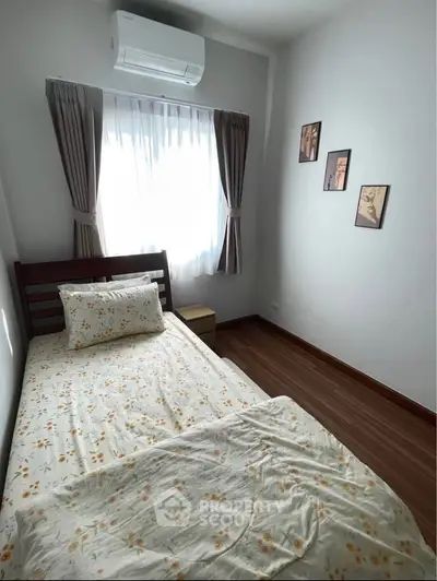 Cozy bedroom with wooden flooring and natural light, featuring a single bed and wall art.