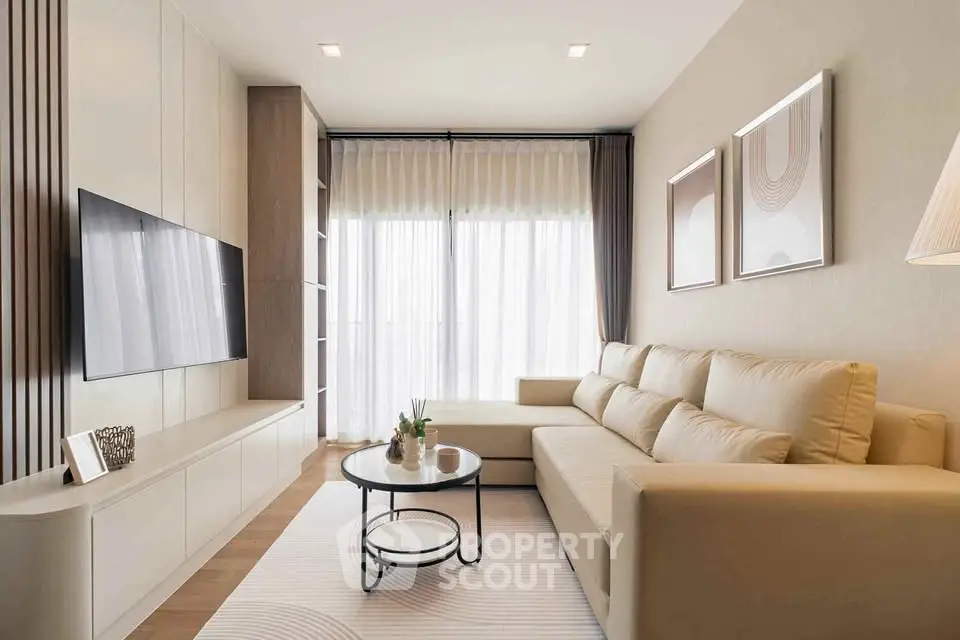 Modern living room with elegant decor and large sofa, featuring a sleek TV setup and natural light.
