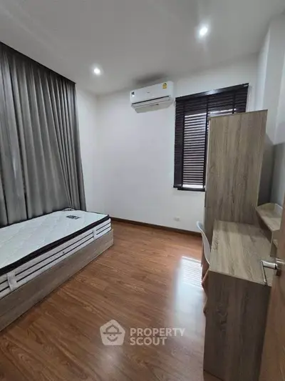 Modern bedroom with wooden flooring, single bed, desk, and air conditioning.