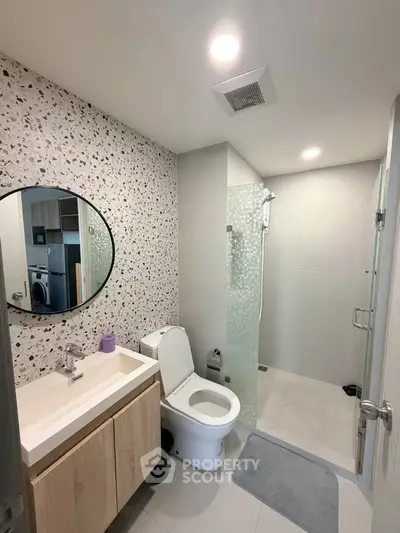 Modern bathroom with terrazzo wall, glass shower, and sleek vanity in contemporary apartment.