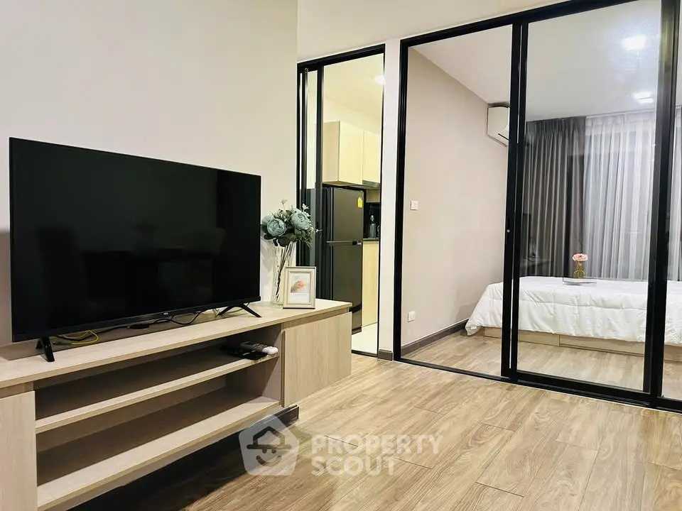Modern living room with TV and view into a cozy bedroom through glass doors.