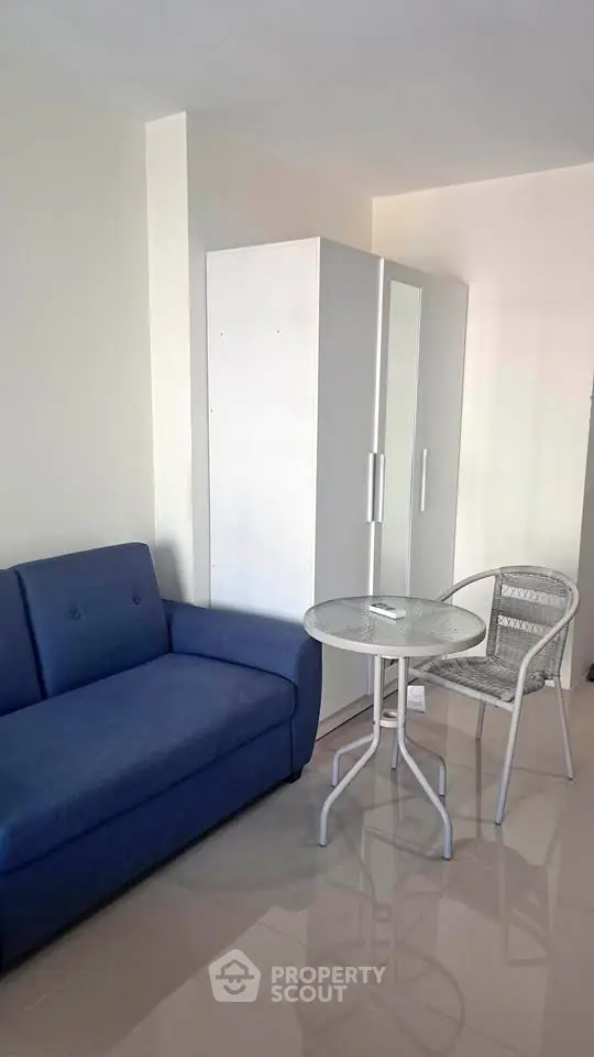 Cozy living room with blue sofa, white wardrobe, and small dining set in modern apartment.