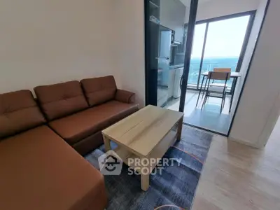 Modern living room with brown sofa and open kitchen leading to balcony with ocean view.