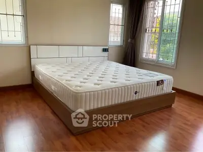 Spacious bedroom with large bed and wooden flooring, featuring ample natural light from windows.