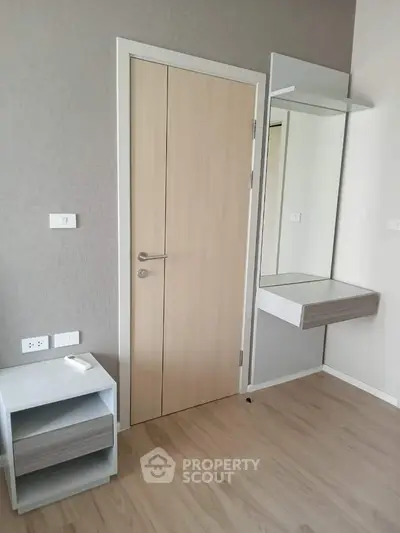 Modern minimalist bedroom with sleek wooden flooring, a large mirror, and a practical floating shelf, offering a serene and spacious atmosphere.