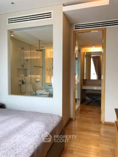 Modern bedroom with ensuite bathroom featuring glass partition and wooden flooring.