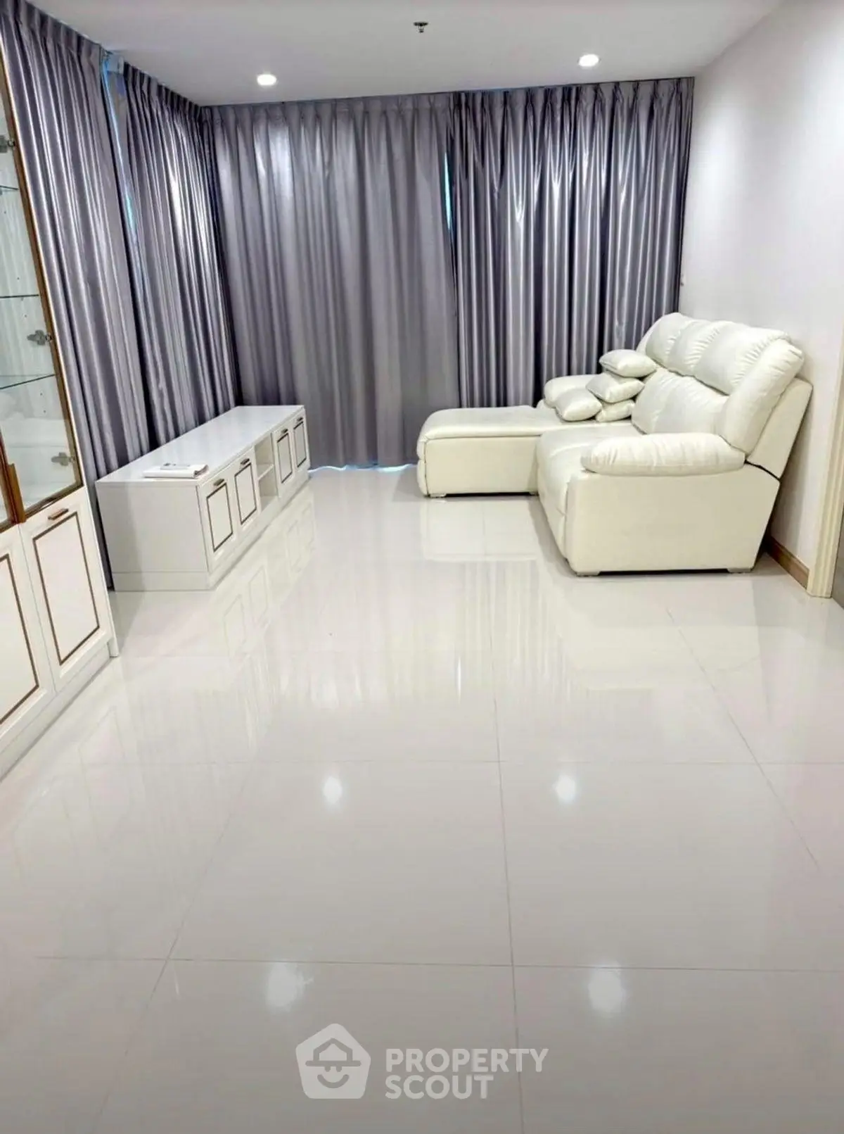 Spacious living room with elegant white leather sofa and floor-to-ceiling curtains.