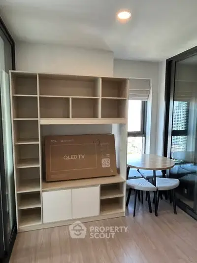 Modern living room with built-in shelving and dining area, featuring a boxed QLED TV.
