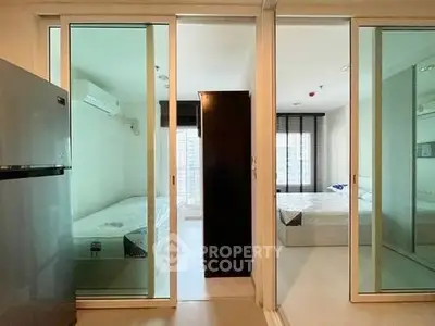 Modern apartment with two bedrooms separated by sliding glass doors and a sleek refrigerator.