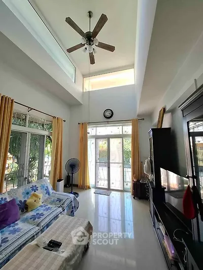Spacious living room with high ceiling and large windows, featuring modern decor and natural light.