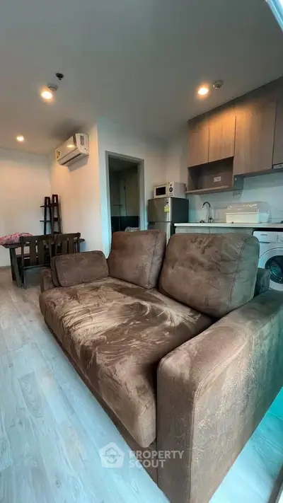 Cozy living room with plush brown sofa and modern kitchen in open layout apartment.