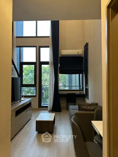 Modern living room with high ceilings and large windows offering natural light and garden view.