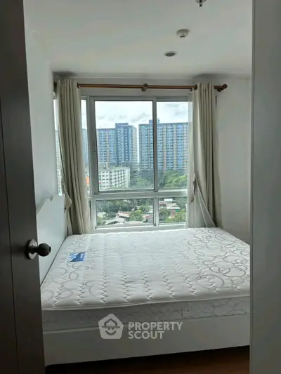 Cozy bedroom with large window offering stunning city views in modern apartment.