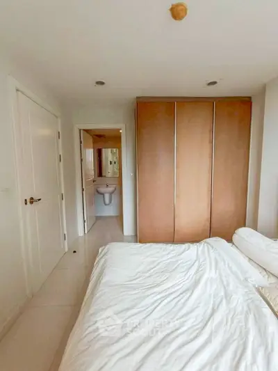 Cozy bedroom with white bedding and wooden wardrobe, leading to a modern en-suite bathroom.