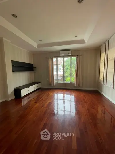 Spacious empty living room with polished wooden floors and large window view.