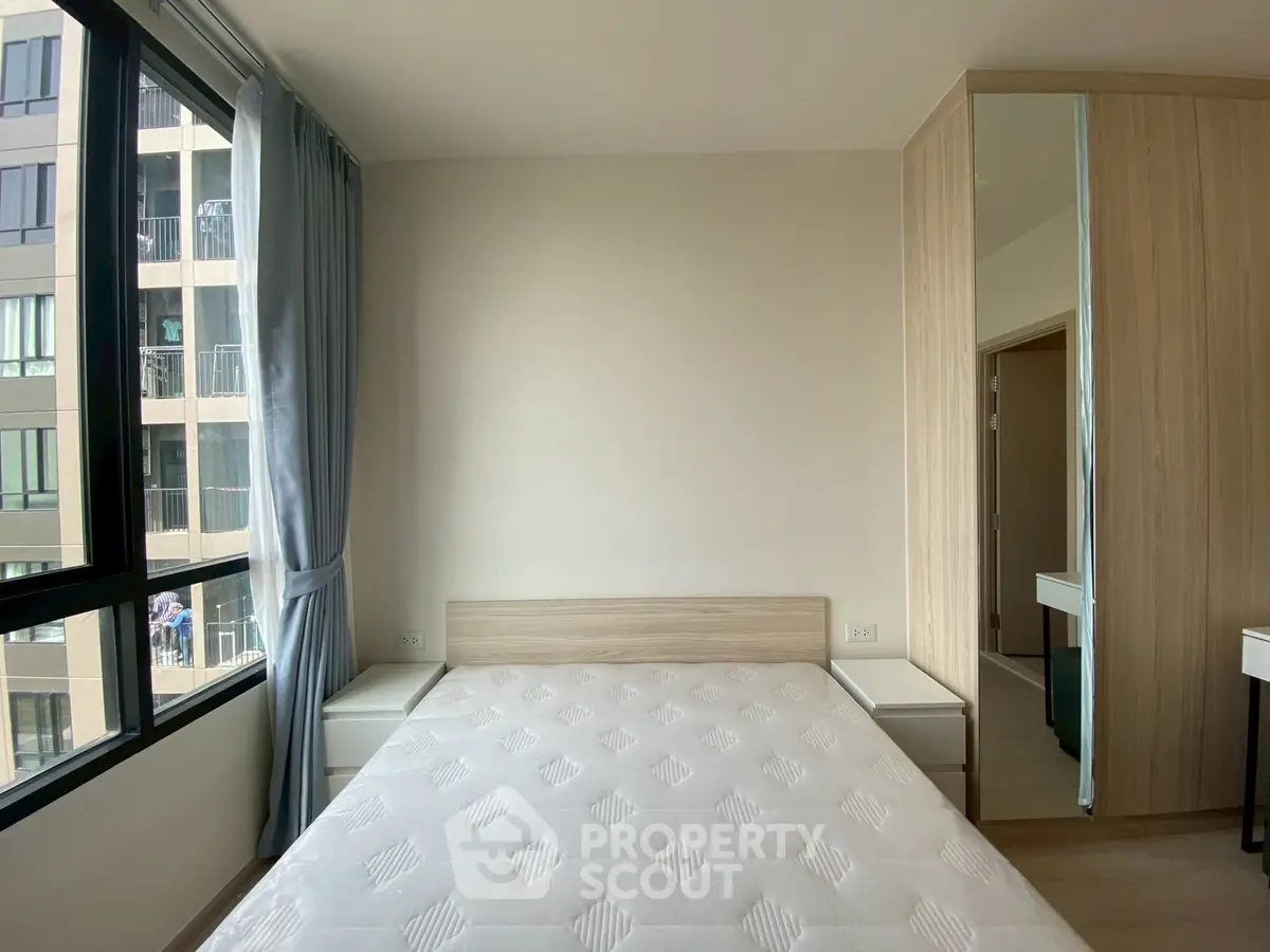 Modern bedroom with large window and built-in wardrobe in a high-rise apartment.