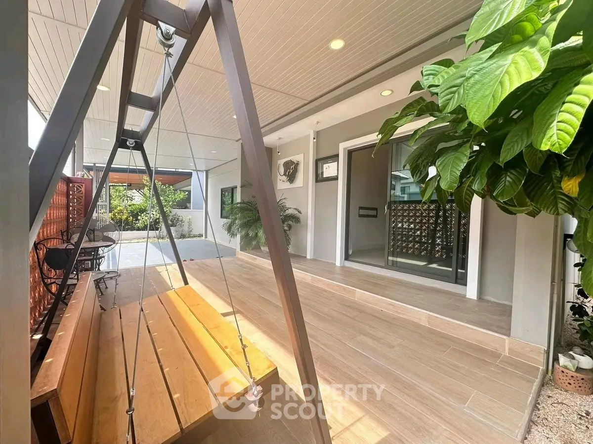 Charming home entrance with cozy swing and lush greenery, perfect for relaxation and welcoming guests.
