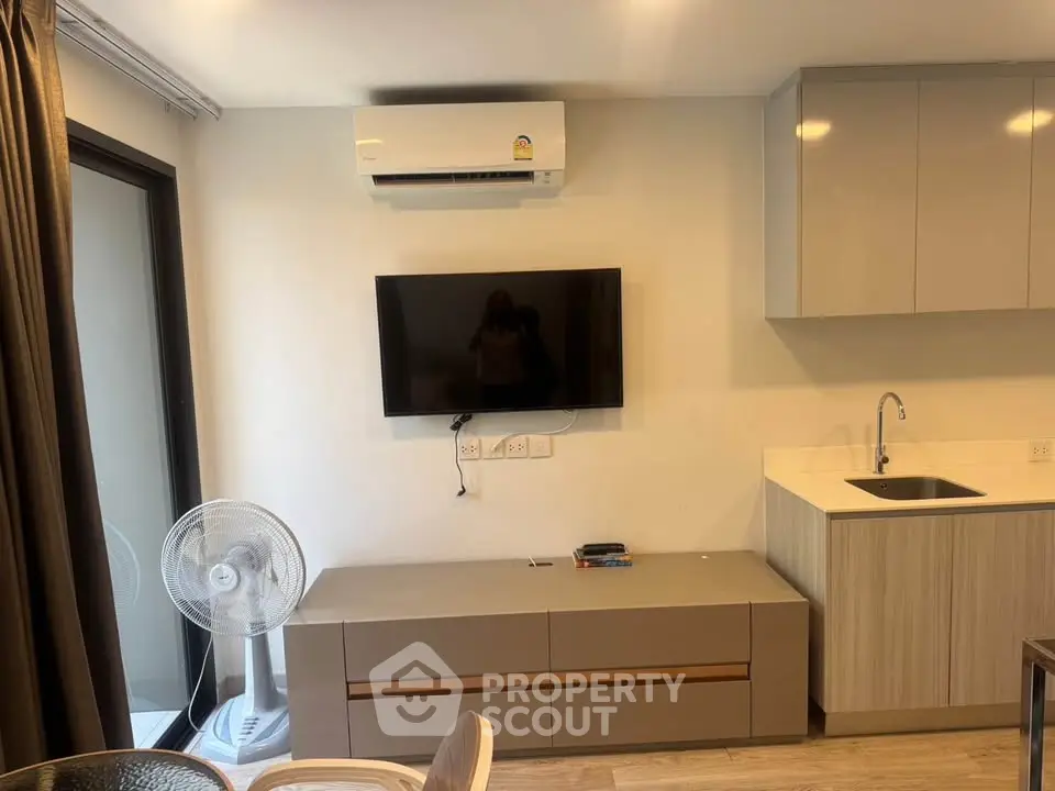 Modern living room with wall-mounted TV and air conditioner, sleek cabinetry, and fan.