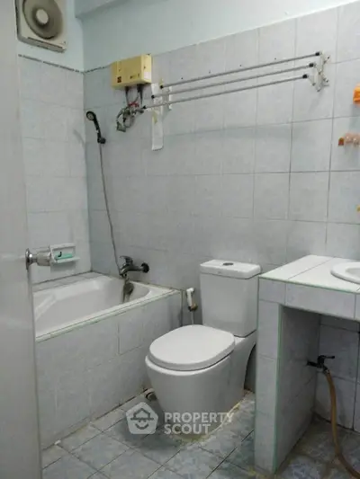 Compact bathroom with bathtub and modern toilet in tiled interior.