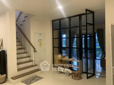Stylish modern living room with glass partition and staircase, featuring sleek design and natural light.