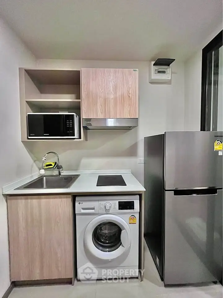 Modern kitchen with washing machine, fridge, and microwave in compact layout.
