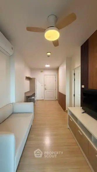 Modern living room with sleek furniture and wooden flooring, featuring a ceiling fan and air conditioning.