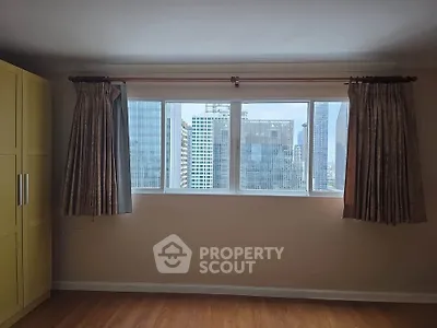 Spacious room with large window offering stunning city skyline view, perfect for urban living.