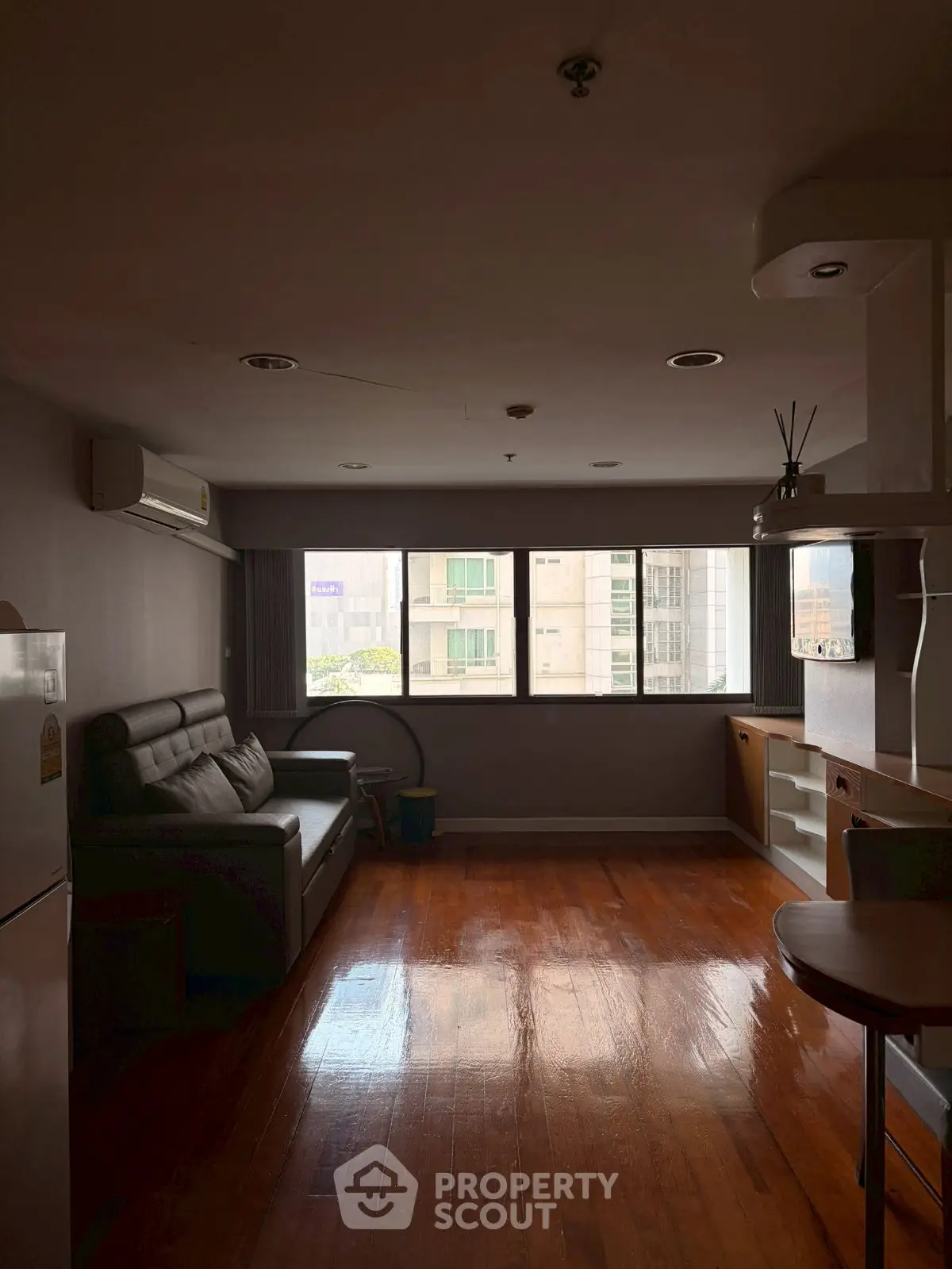 Spacious living room with wooden flooring and large windows offering city views.