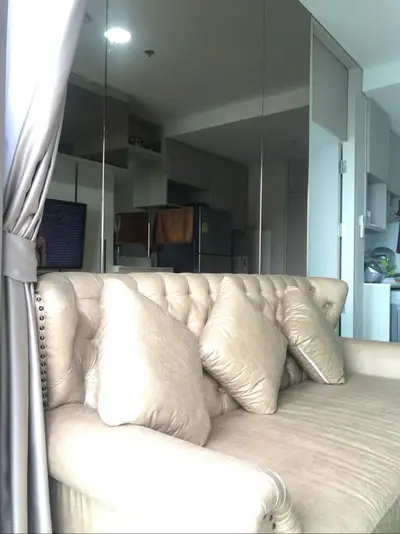 Modern living room with plush beige sofa and mirrored wall, open kitchen layout in background.