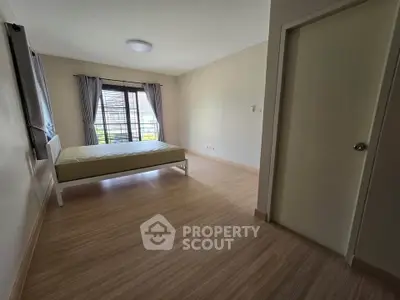 Spacious bedroom with wooden flooring and large window for natural light.