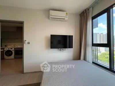 Modern bedroom with wall-mounted TV and city view, adjacent to a kitchen with appliances.