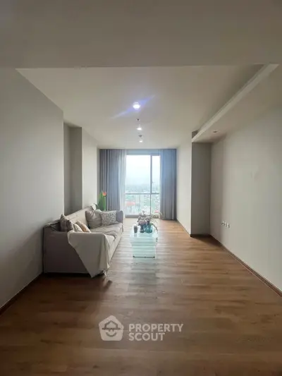 Spacious living room with wooden flooring and city view through large window.