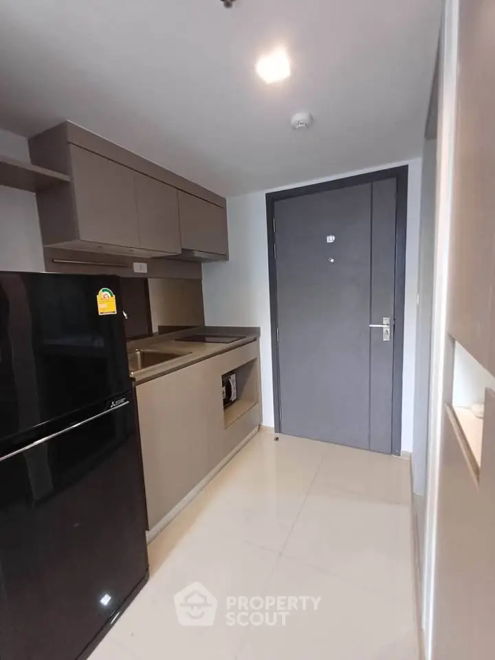 Modern compact kitchen with sleek cabinetry and black refrigerator in a stylish apartment.