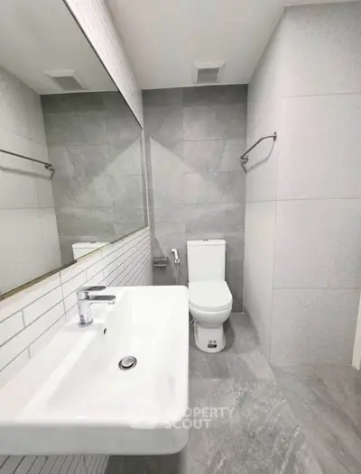 Modern bathroom with sleek design, featuring a white sink and toilet against gray tiled walls.