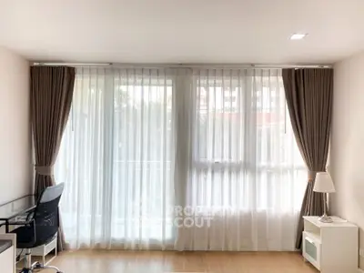 Spacious and well-lit living room with elegant floor-to-ceiling curtains, hardwood flooring, and tasteful furnishings, ideal for comfortable urban living.