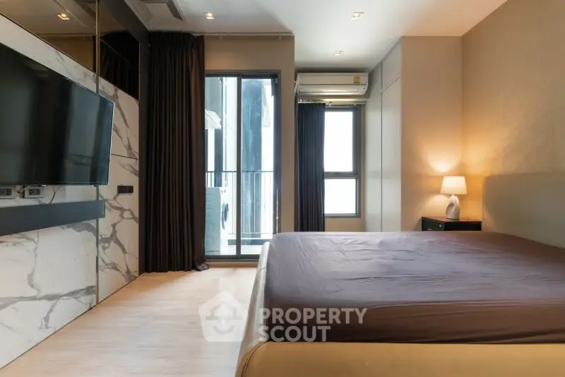 Modern bedroom with sleek design and large TV, featuring floor-to-ceiling windows and elegant lighting.