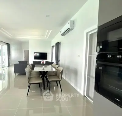 Modern living room with sleek dining area and built-in oven, featuring minimalist design and ample natural light.