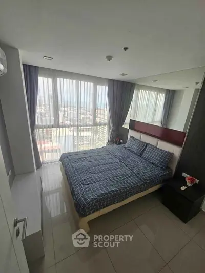 Spacious bedroom with large windows offering stunning city views, modern decor, and ample natural light.