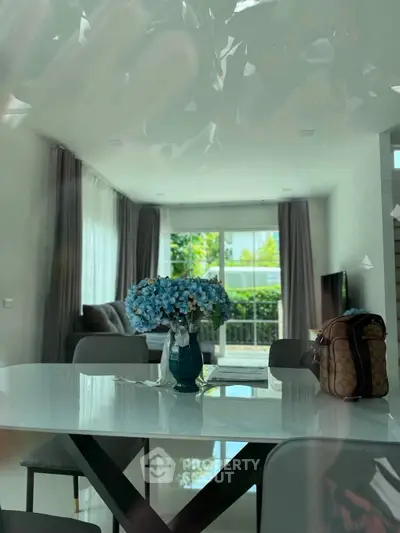 Modern living room with elegant dining table and lush garden view through large windows.