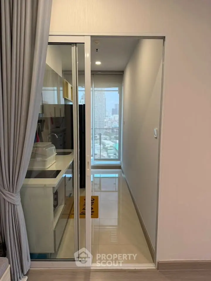 Modern apartment with sleek kitchen and city view, featuring sliding glass doors and elegant flooring.