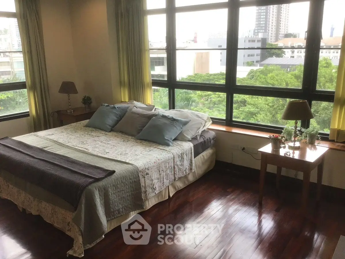 Spacious bedroom with large windows offering a stunning city view, featuring elegant decor and hardwood floors.