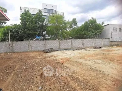 Vacant land plot with potential for development, surrounded by trees and adjacent to a modern building.