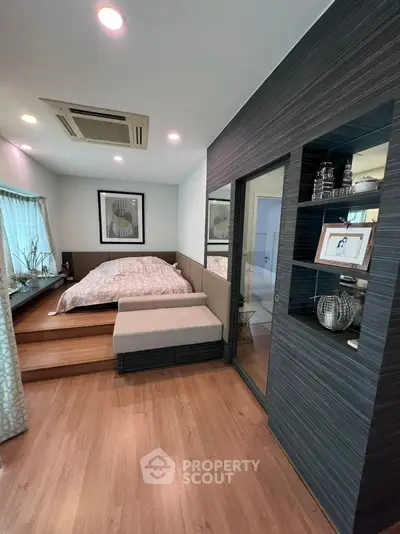 Modern bedroom with stylish decor and wooden flooring, featuring a cozy bed and elegant shelving.