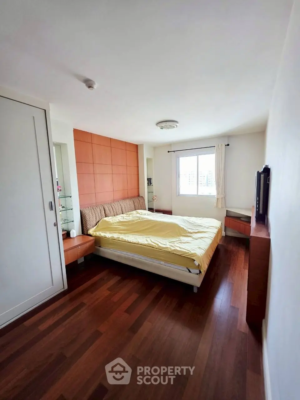 Spacious bedroom with wooden flooring and large window for natural light