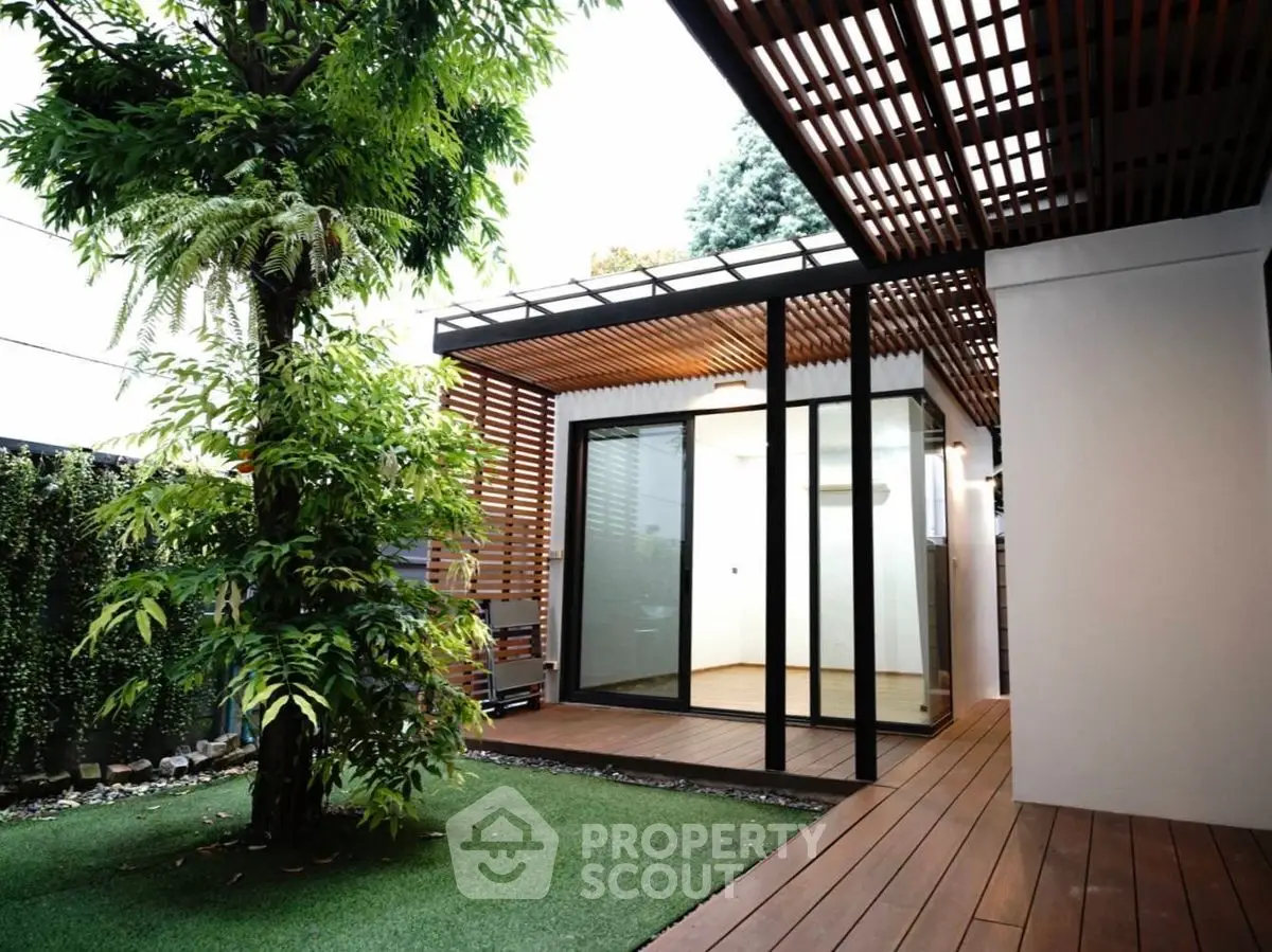 Modern garden view with wooden deck and glass-walled room, perfect for relaxation.