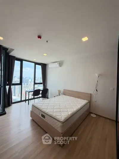 Spacious bedroom with city view and modern furnishings in high-rise apartment.