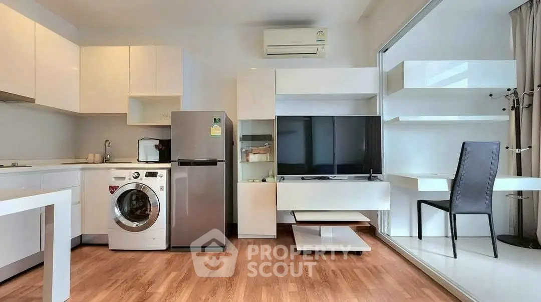 Modern open-layout living room with kitchen, featuring washing machine and sleek furniture.