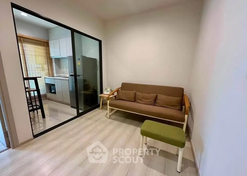 Cozy living room with modern kitchen view, featuring sleek glass partition and stylish furniture.