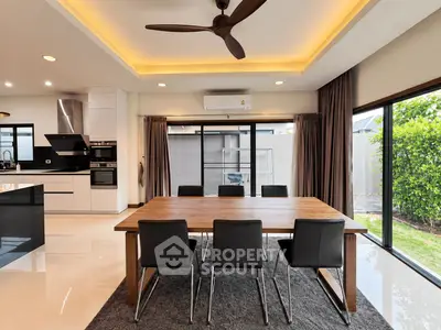 Modern dining area with sleek table, chairs, and open kitchen layout, featuring large windows and garden view.