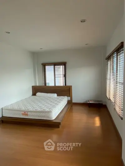 Spacious bedroom with wooden flooring and large windows for natural light.